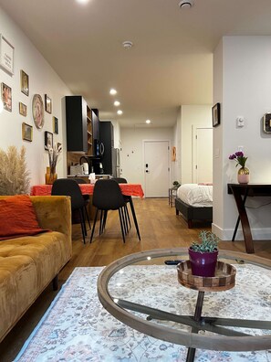 Uma sala de estar moderna com sofá, um espaço de refeições com cadeiras, uma cozinha, uma cama e uma pequena mesa com um vaso.