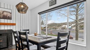 A dining area with a large window, a fireplace, and a view of a snowy landscape. - Modern Brian Head Condo - Walk to Giant Steps -  Hot Tub - Pet Friendly (Brian Head)