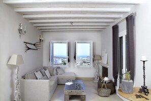 A living room with a sofa, a coffee table, two windows with a view, a fireplace, and a lamp. - Villa Mirethiax, Divine Sea Views, Furnished Terrace, Tinos (Tinos)