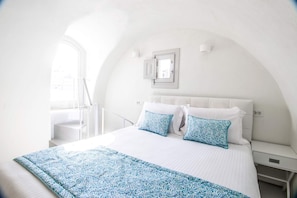 Ein Schlafzimmer mit Bett, weißen Wänden, einem Fenster und einer Treppe.