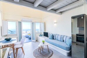 Ein modernes Wohnzimmer mit Sofa, Esstisch, Stühlen, einem kleinen Tisch mit Pflanze und einer Küchenzeile mit Backofen.