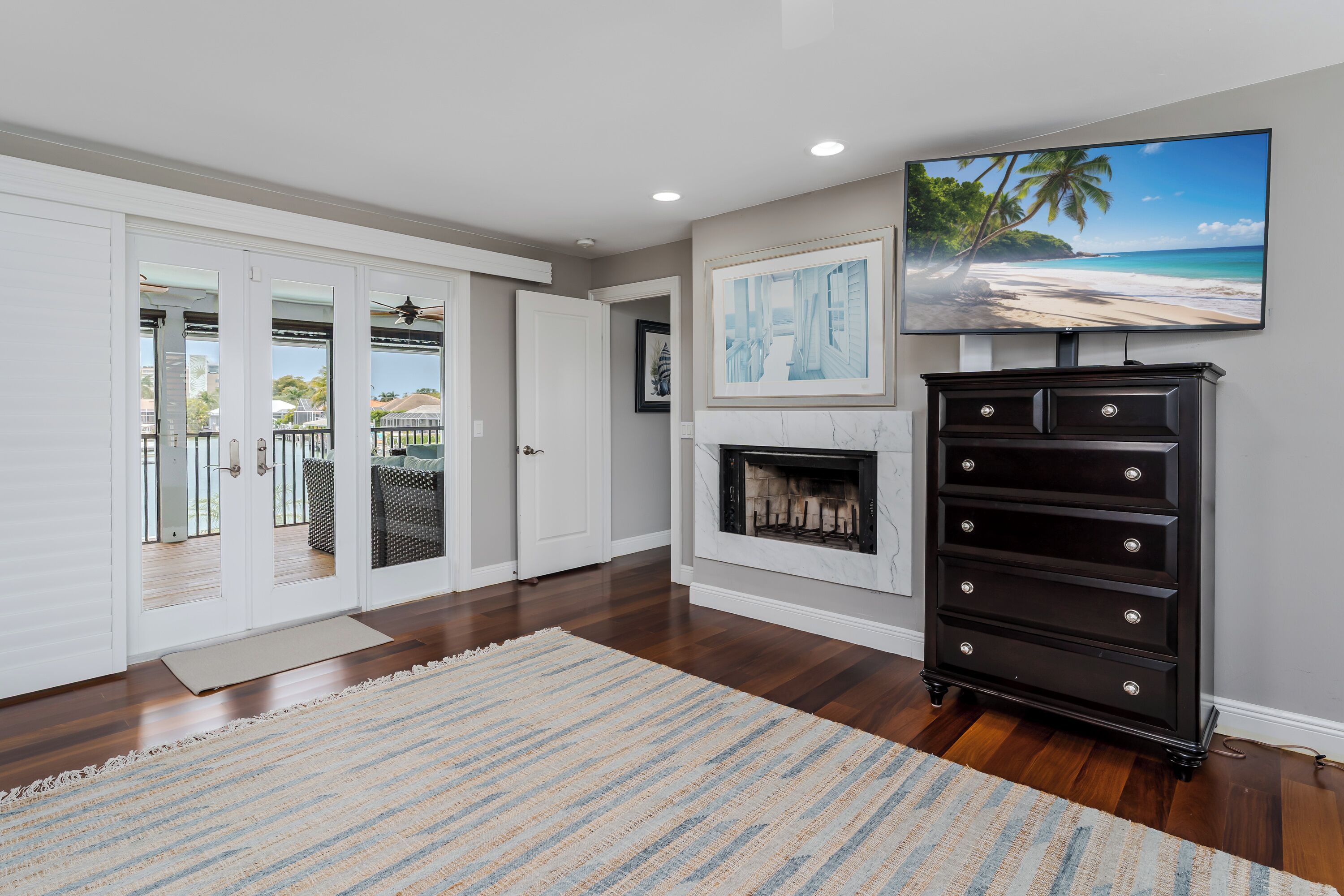 A spacious room with a fireplace, a large TV, and a view of a beach through the glass doors.