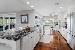 A modern kitchen with white cabinets, a granite countertop, and a view to the outside. - Grand Canalside Direct access 2 blocks to beach (Marco Island)