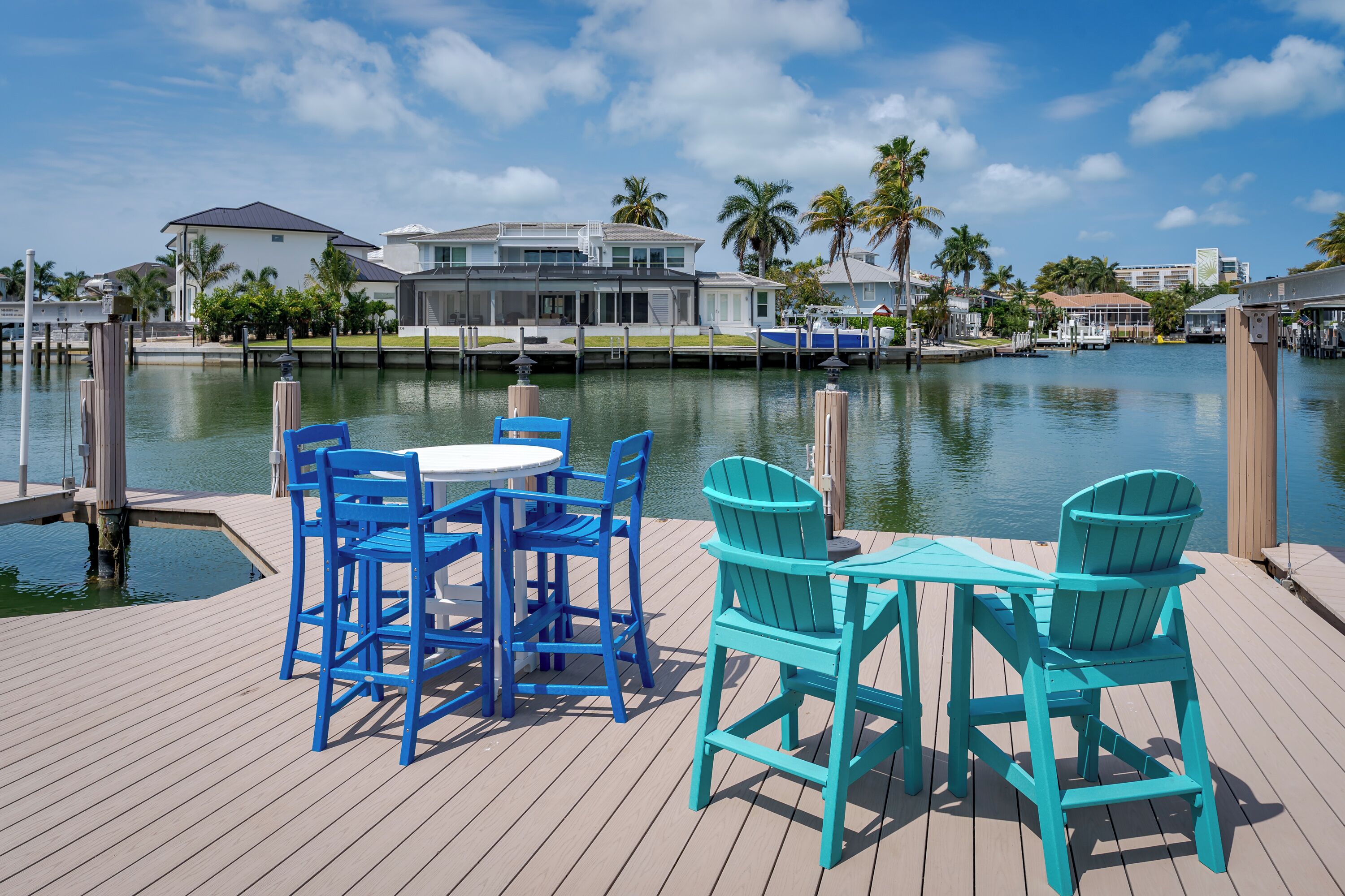 A waterfront property with a dock, a table with chairs, and a view of a house across the water.