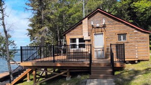 A cabin with a deck, a garage, and a view of the water. - Cozy Retreat For Two (Greater Sudbury)