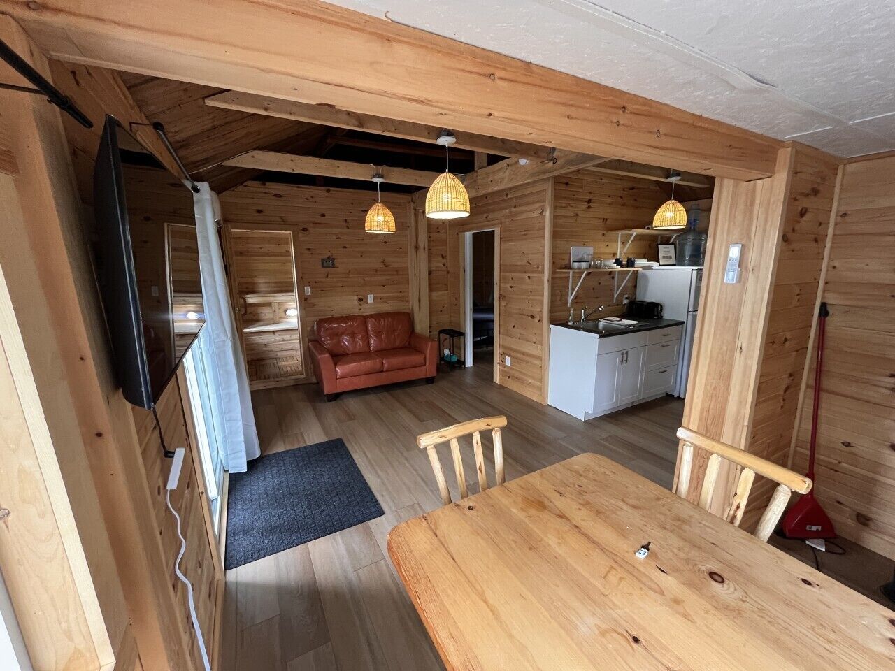A wooden interior with a dining table, chairs, a sofa, and a kitchen area.