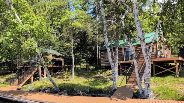 A lakeside cabin with a dock, surrounded by trees and a grassy area. - Cozy Retreat For Two (Greater Sudbury)