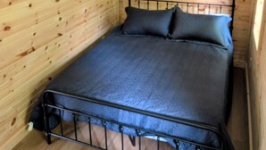 A small, single-bed room with wooden walls and a metal bed frame. - Cozy Retreat For Two (Greater Sudbury)
