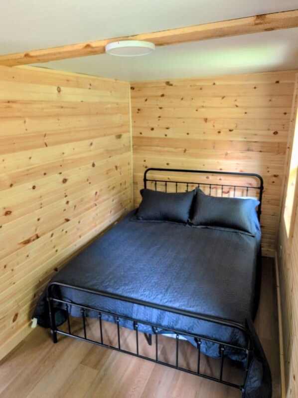 A small, single-bed room with wooden walls and a metal bed frame. - Cozy Retreat For Two (Greater Sudbury)