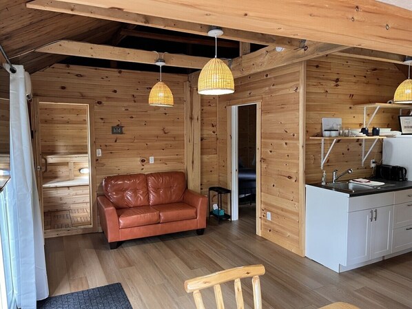 Un accogliente interno di una baita con un divano in pelle, pareti in legno e un angolo cottura.
