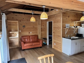 A cozy cabin interior with a leather sofa, wooden walls, and a kitchenette.