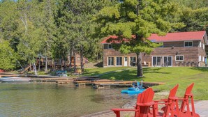 A lakeside cabin with a dock, red Adirondack chairs, and a boat. - Fairbank Lake Cottages - Main Lodge (Whitefish)