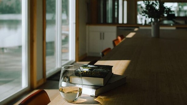 A long table with chairs, a glass, and a book, with windows along one side. - Fairbank Lake Cottages - Main Lodge (Whitefish)
