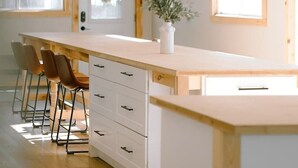 A modern kitchen with a wooden island, bar stools, and a vase with greenery. - Fairbank Lake Cottages - Main Lodge (Whitefish)