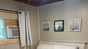 Un llit amb un edredó blanc acolxat, un panell de capçal blanc i una finestra amb un aparell d'aire condicionat.