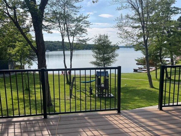 A deck with a view of a lake, surrounded by trees and a grassy area with a grill.
