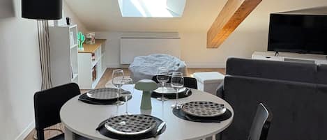 A dining area with a round table set for four, a TV, and a wooden ceiling beam.