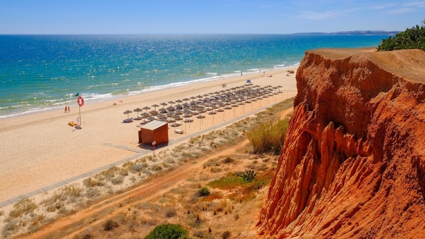 A beach with a clear view of the ocean, a sandy path, and a rocky cliff. - Marina Luxor 21 in Vilamoura (Loulé)