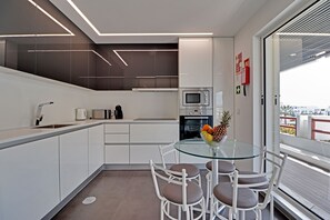 A modern kitchen with white cabinetry, a glass dining table, and a view through a large window. - Marina Luxor 21 in Vilamoura (Loulé)