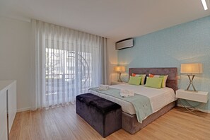 A bedroom with a bed, bedside lamps, a window with curtains, a wall-mounted air conditioner, and a wooden floor. - Marina Luxor 21 in Vilamoura (Loulé)
