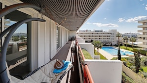 A balcony with a view of a swimming pool, a hat, and a towel. - Marina Luxor 21 in Vilamoura (Loulé)