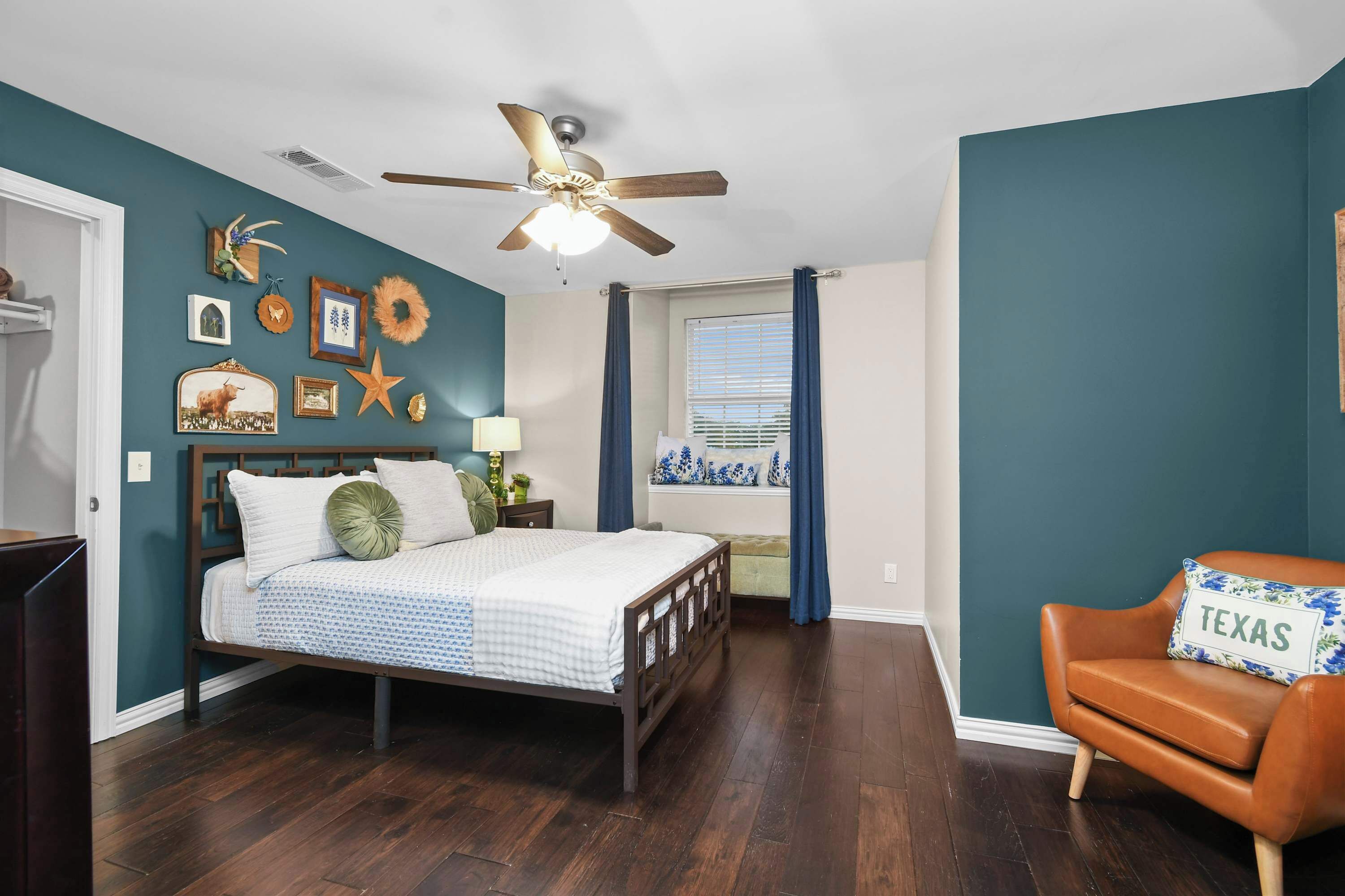 A bedroom with a bed, a ceiling fan, a window with curtains, and a chair with a pillow.