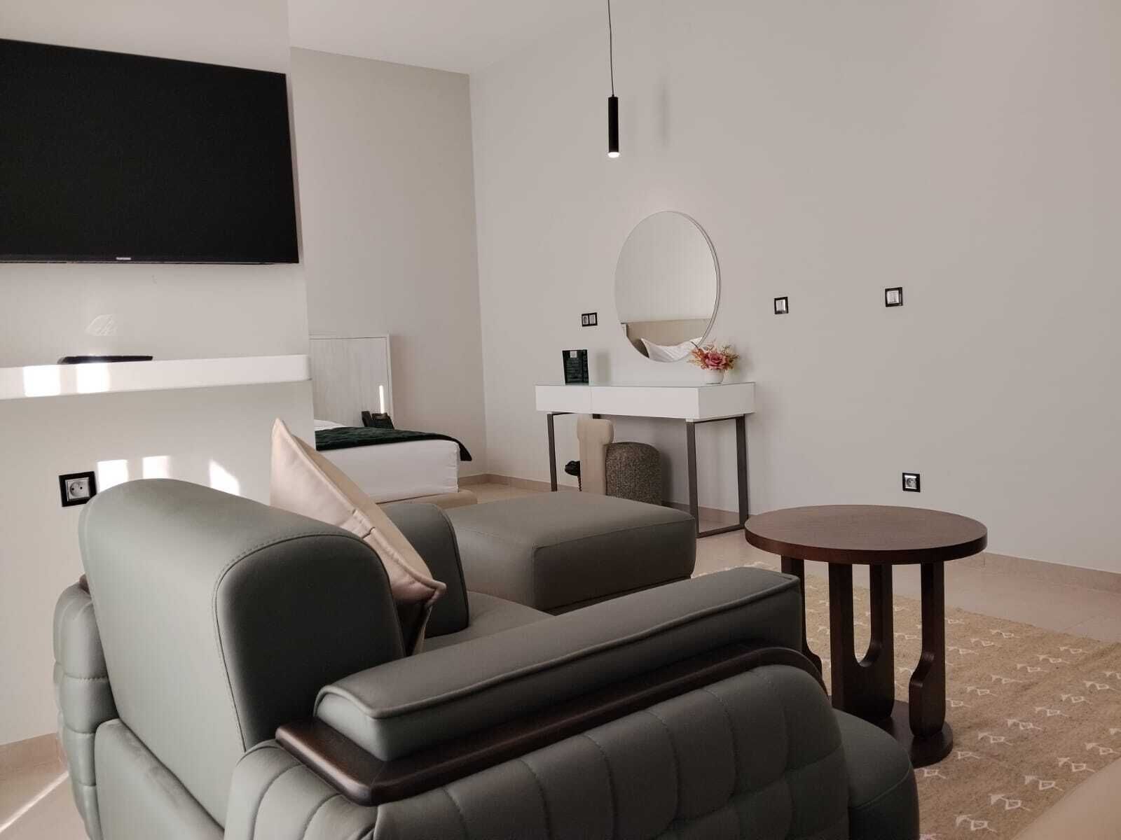 A modern living room with a sofa, a round coffee table, a TV mounted on the wall, and a small round table with a mirror.