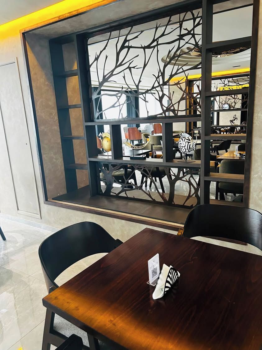 A dining area with a wooden table and chairs, a decorative window with a tree motif, and a view of the street outside.