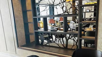 A dining area with a wooden table and chairs, a decorative window with a tree motif, and a view of the street outside.