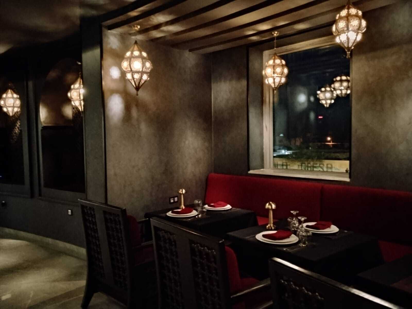 A dimly lit restaurant with tables set for dining, a red cushioned bench, and hanging light fixtures.