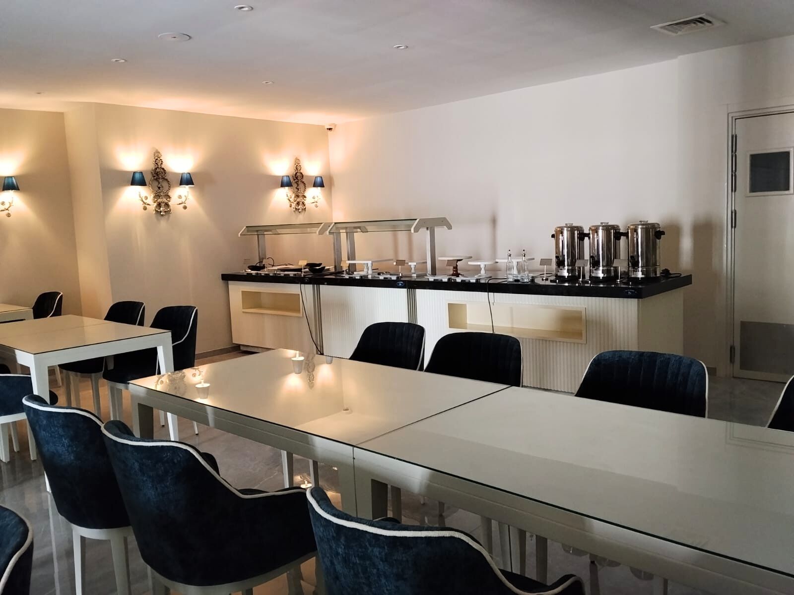 A conference room with a long table, chairs, a coffee station, and wall-mounted lighting.