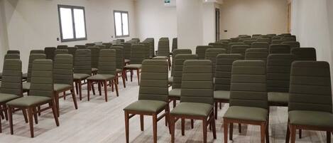 Une salle de conférence avec des rangées de chaises vertes et des tables en bois, des murs blancs et des luminaires au plafond.