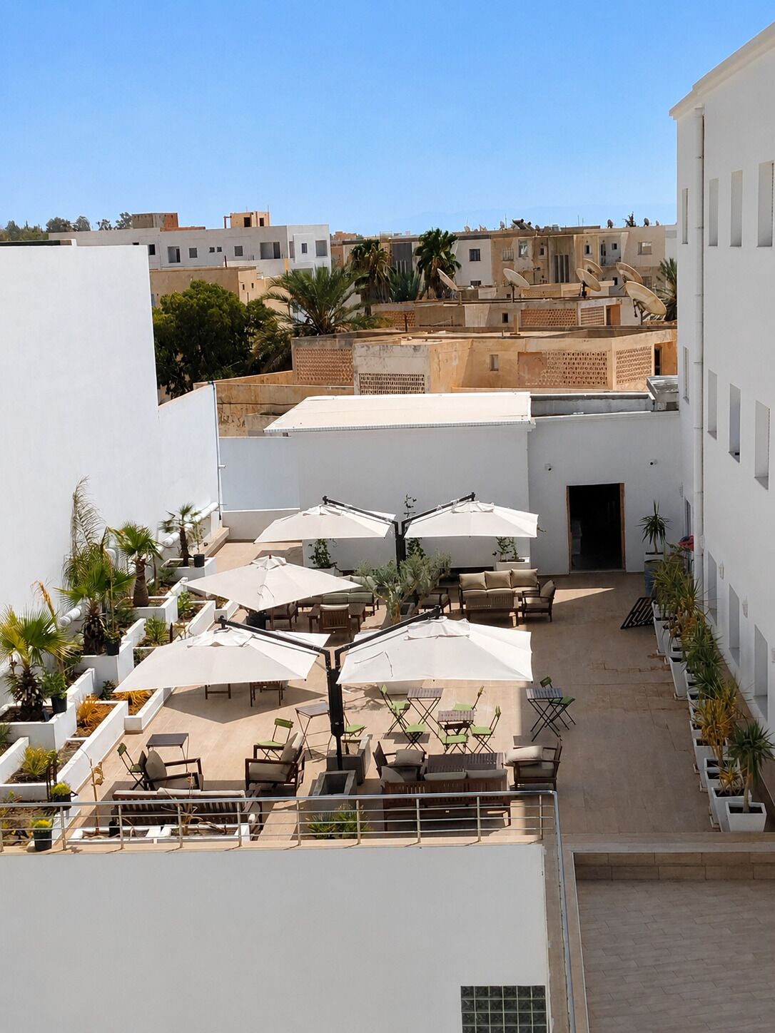 Una terraza en la azotea con mobiliario exterior, sombrillas blancas y plantas en macetas.