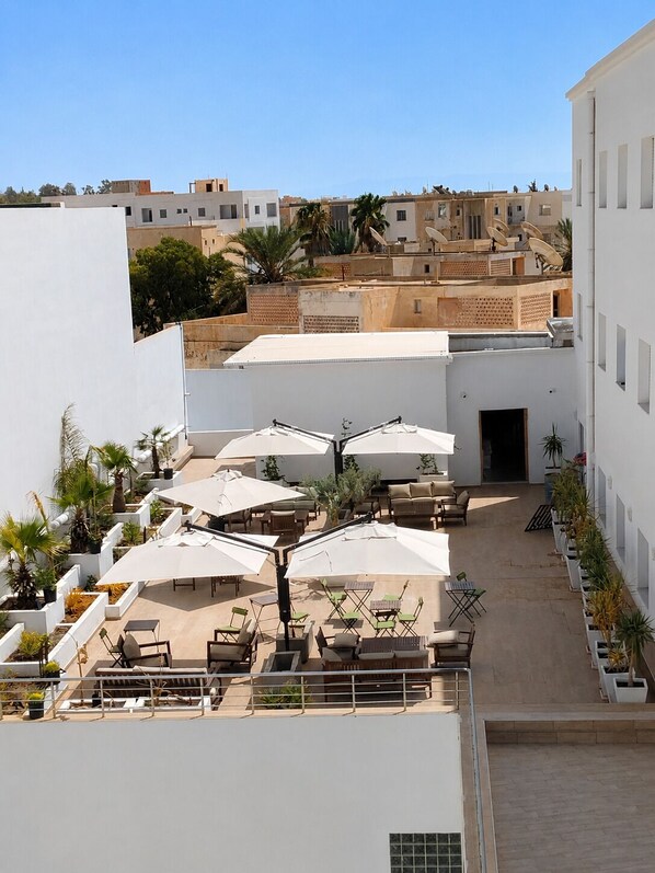 Una terraza en la azotea con mobiliario exterior, sombrillas blancas y plantas en macetas.
