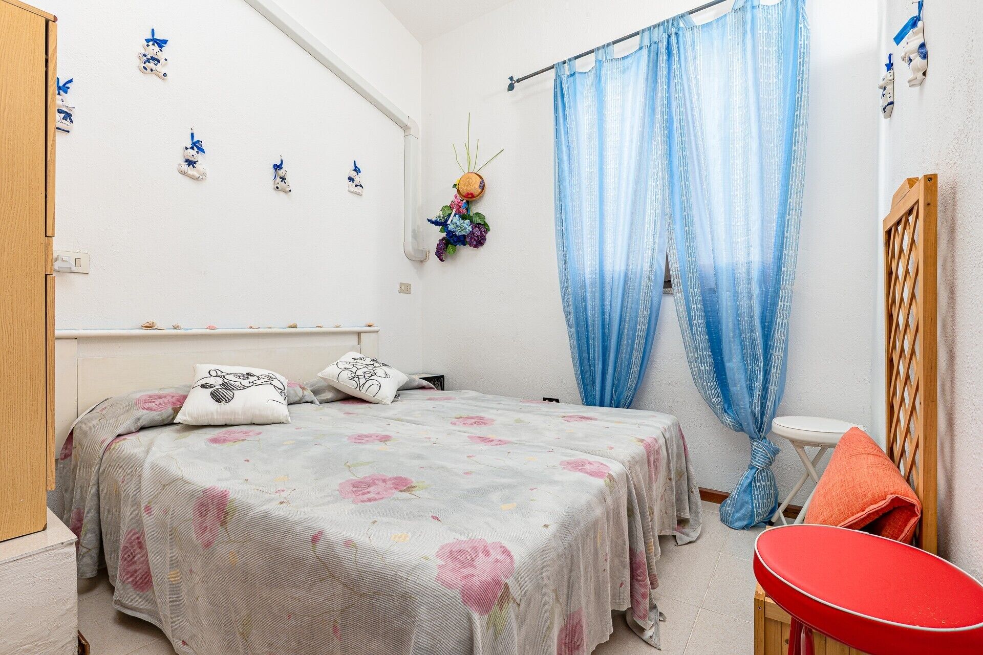 Un dormitorio con una cama, una silla roja, un armario de madera y una cortina azul.