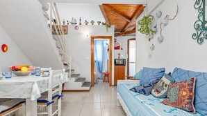 A cozy interior with a dining area, a staircase, a sofa with patterned cushions, and a kitchen area. - Apartment 'Del Tirreno' with Private Terrace and Air Conditioning (San Teodoro)