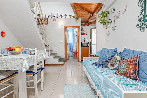Ein gemütliches Interieur mit Essbereich, Treppe, einer Couch mit gemusterten Kissen und einer Küchenzeile.