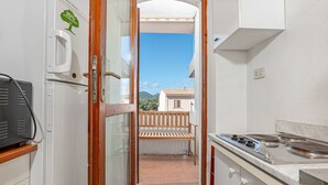 A narrow kitchen with a view to a balcony, a stove, and a refrigerator. - Apartment 'Del Tirreno' with Private Terrace and Air Conditioning (San Teodoro)