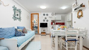 A compact living space with a sofa, dining table, chairs, a TV, and a kitchen area. - Apartment 'Del Tirreno' with Private Terrace and Air Conditioning (San Teodoro)