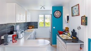 Una cocina moderna con armarios blancos, horno empotrado, lavabo y ventana con vistas a zonas verdes.