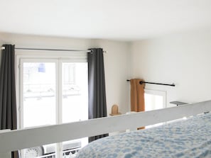 Ein Zimmer mit Bett, einem Vorhangfenster, einer Tür und Blick nach draußen.