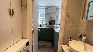 A compact bathroom with a washing machine, a sink, and a mirror. - Putney: Chic Flat, River & Tube (London)