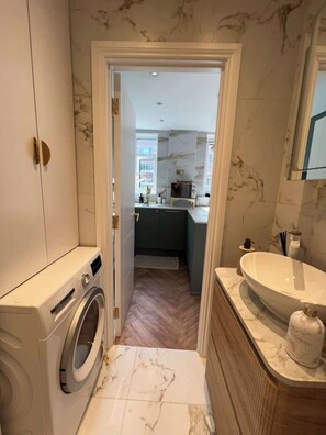 A compact bathroom with a washing machine, a sink, and a mirror. - Putney: Chic Flat, River & Tube (London)