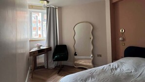 A bedroom with a bed, a desk, a chair, a mirror, and a window with curtains. - Putney: Chic Flat, River & Tube (London)