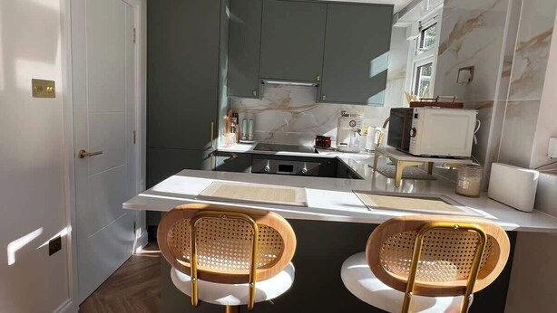 A modern kitchen with two bar stools, a white countertop, and a pendant light. - Putney: Chic Flat, River & Tube (London)