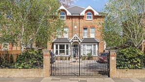 A two-story brick house with a gated driveway, a small front garden, and a garage. - Spacious 5-Bed Family Home with Garden & Parking (London)