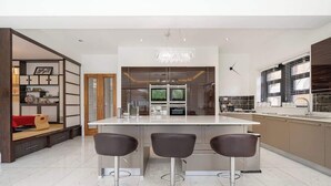 A modern kitchen with a central island, three bar stools, and a chandelier. - Spacious 5-Bed Family Home with Garden & Parking (London)
