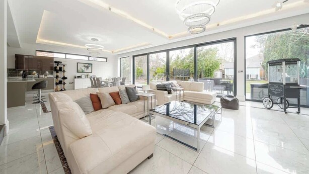 A modern living room with a sofa, coffee table, and a kitchen in the background. - Spacious 5-Bed Family Home with Garden & Parking (London)