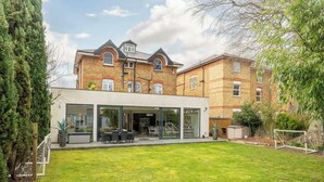 A modern two-story house with a well-maintained lawn, a patio with outdoor furniture, and a visible garage. - Spacious 5-Bed Family Home with Garden & Parking (London)