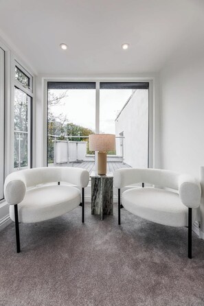 A modern room with two white armchairs, a marble side table, and a large window with a view of a garden. - Designer 4-Bed, Skyline Views & Free Parking (London)